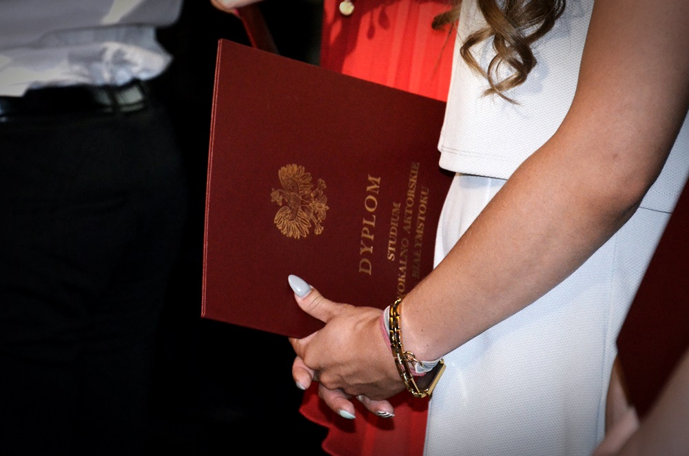 Uczennica w białej sukience trzyma dyplom