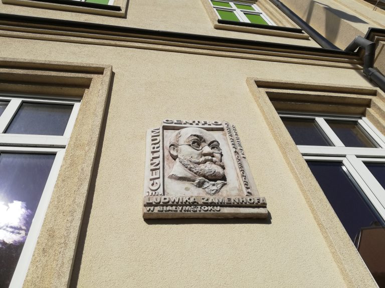 Fragment zewnętrznej ściany, w piaskowym kolorze, na której znajduje się płaskorzeźba ukazująca twarz Ludwika Zamenhofa