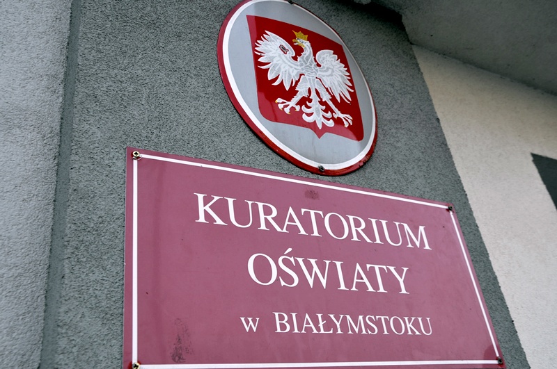 Na czerwonej tabliczce jest napisane: Kuratorium Oświaty w Białymstoku. Nad tabliczką wisi godło Polski