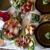 Stół nakryty białym obrusem , a nim stoją wędliny, jajka, sery