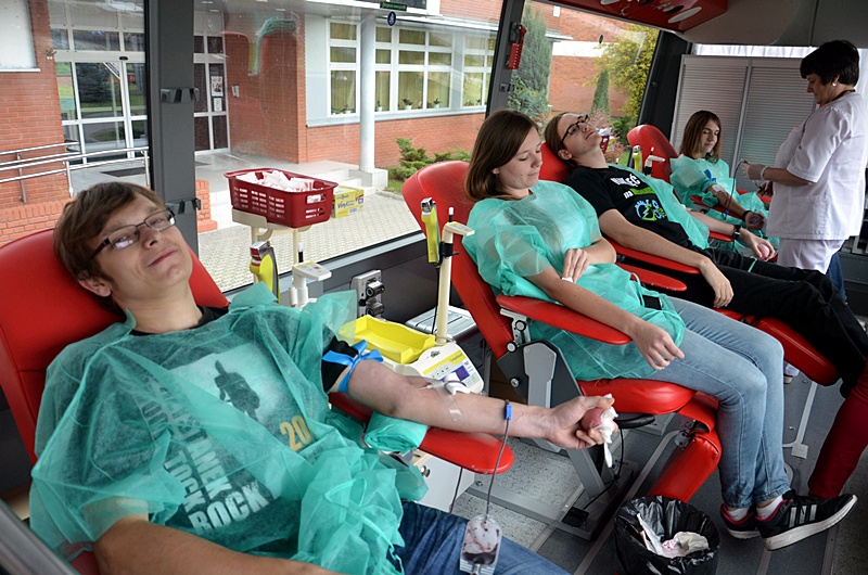 Kilka osób siedzi na fotelach w jednorazowych fartuchach i oddaje krew