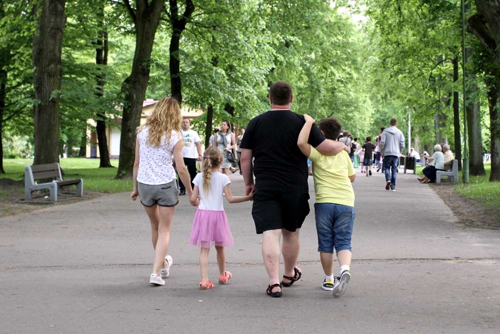 Rodzice z dziećmi idą przez park
