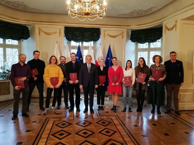 Grupka ludzi stoi w pomieszczeniu Pałacyku Gościnnego, w środku stoi prezydent