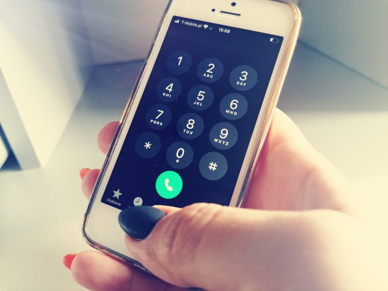Biały telefon komórkowy trzymany jest w dłoni