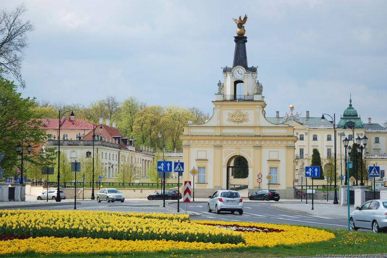 Brama Pałacu Branickich widziana za rondem obsadzonym kolorowymi kwiatami.