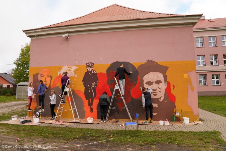 grupa młodzieży maluje mural na ścianie budynku
