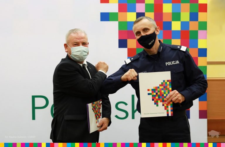 Marszałek Olbryś i gen. Szewc stykają się łokciami zamiast podania rąk. Generał trzyma w drugiej ręce teczkę z umową