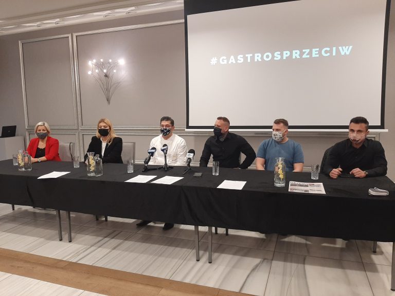 Przy długim stole siedzi kilka osób. Za nimi na rzutniki widoczny jest napis Gastrosprzeciw