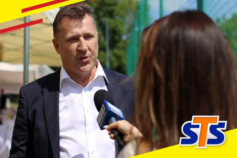 Mężczyzna w garniturze odpowiada na pytania dziennikarki telewizyjnej do mikrofonu z logo stacji.