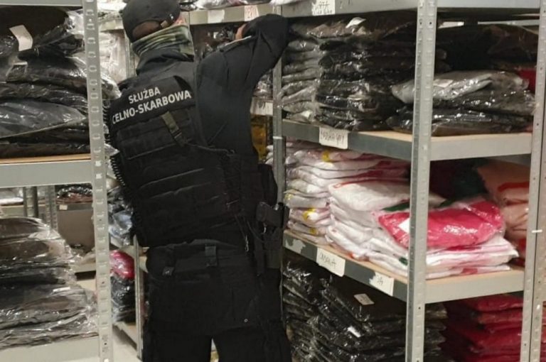 Oficer podlaskiej KAS stoi przy regale, na którego półkach leżą materiały tekstylne.