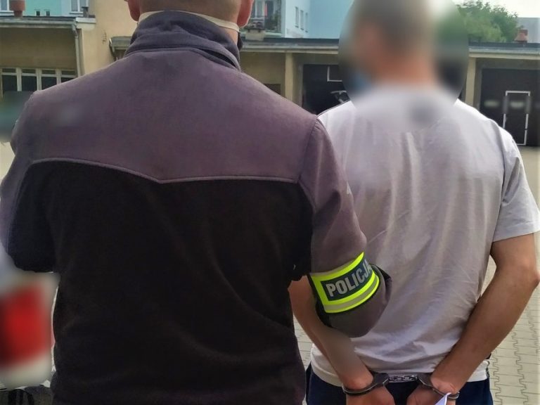 Policjant trzyma za rękę skutego mężczyznę.