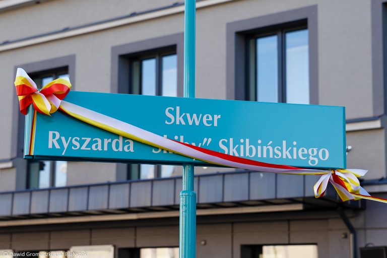 Niebieska tabliczka z nazwą skweru ryszarda skiby skibińskiego przepasana trójkolorową kokardą
