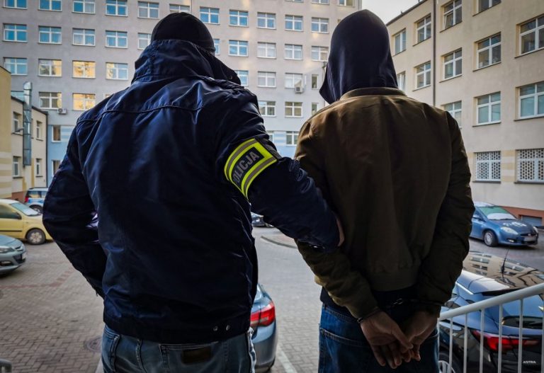 Policjant trzyma skutego kajdankami mężczyznę