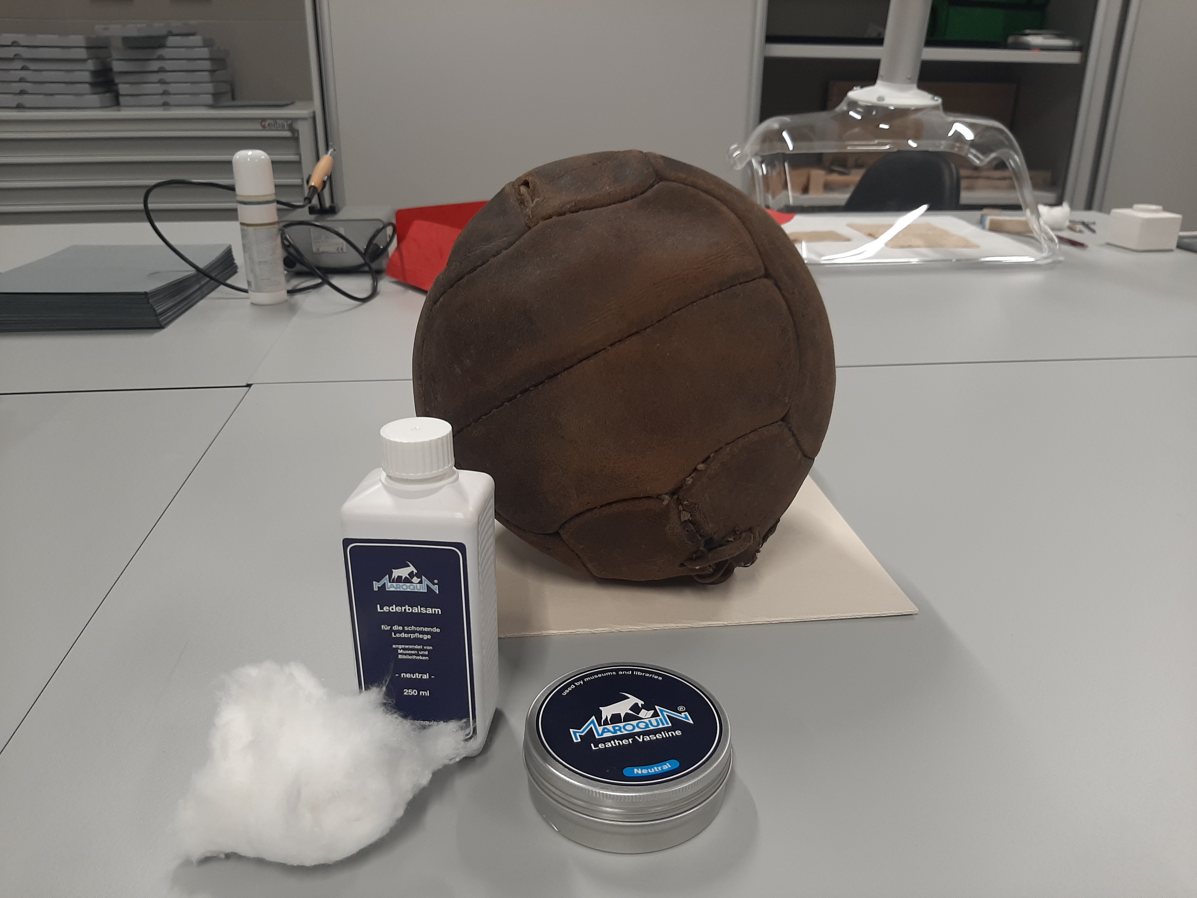 Pracowni konserwatorska. Na stole leży piłka z międzywojnia, przed nią stoją preparaty do konserwacji