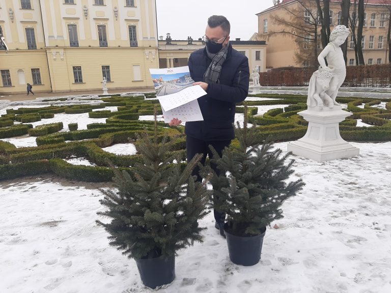 W parku Pałacu Branickich, przy jednej z rzeźb stoi zastępca prezydenta i prezentuje kalendarz ścienny, w którym przekłada kartki. Przed mężczyzną stoją dwa świerki w doniczce, a nim widoczny jest fragment Pałacu Branickich