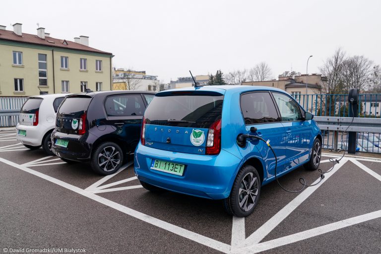 Na parkingu za Urzędem Miejskim w Białymstoku przy ul. Słonimskiej stoją trzy auta elektryczne. Od lewej strony stoi samochód biały, pośrodku czarny, z prawej niebieski