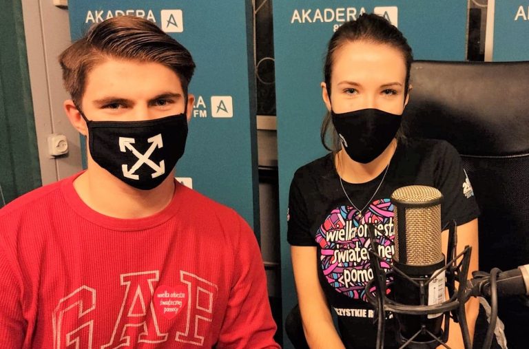 Mężczyzna i kobieta siedzą przed mirofonem w radiowym studiu. Na twarzy mają maseczki