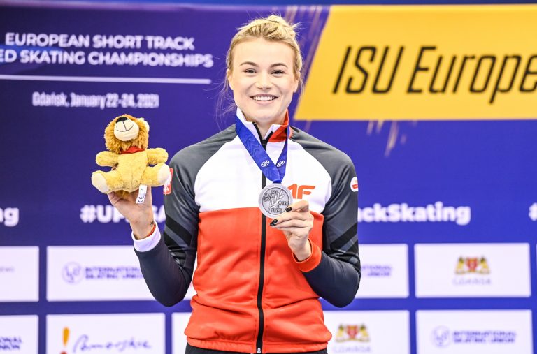 Natalia Maliszewska prezentuje srebrny medal. Krążek ma zawieszony na szyi i trzyma go w lewej ręce, natomiast w prawej ma pluszowego lwa