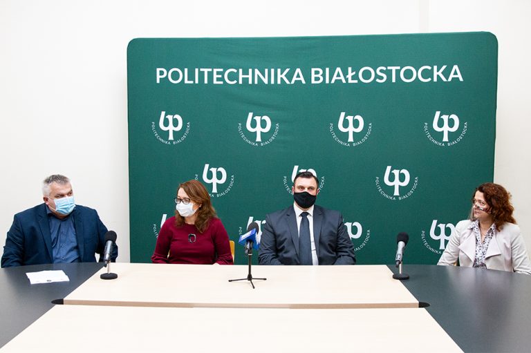 Na tle zielonej ścianki Politechniki Białostockiej siedzą cztery osoby