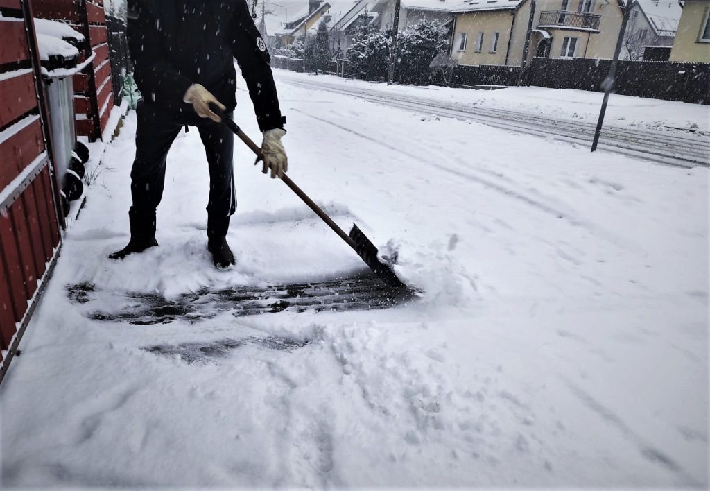 Mężczyzna odśnieża zasypany śniegiem chodnik