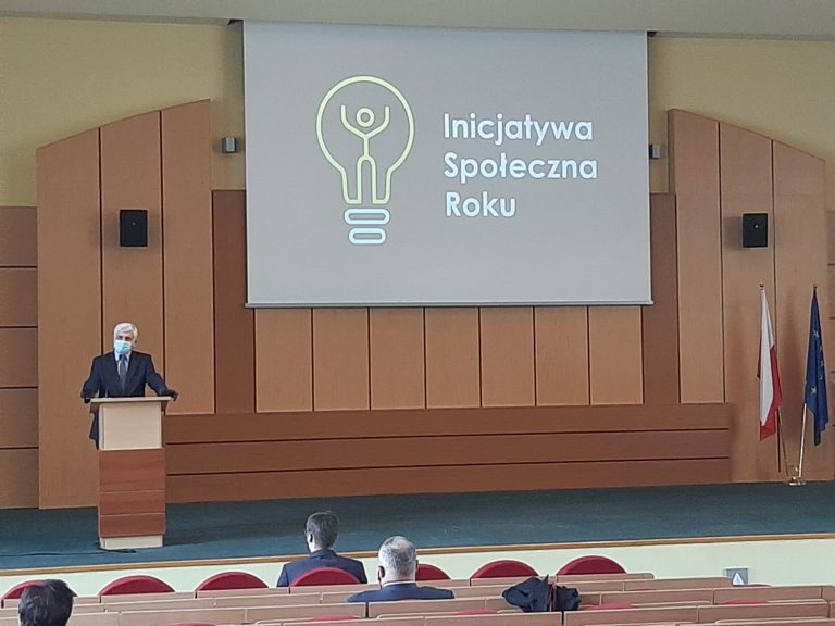 Sala konferencyjna Podlaskiego Urzędu Wojewódzkiego. Przy mównicy stoi wojewoda. Na ścianie znajduje się rzutnik, na którym jest wyświetlony napis Inicjatywa Społeczna Roku