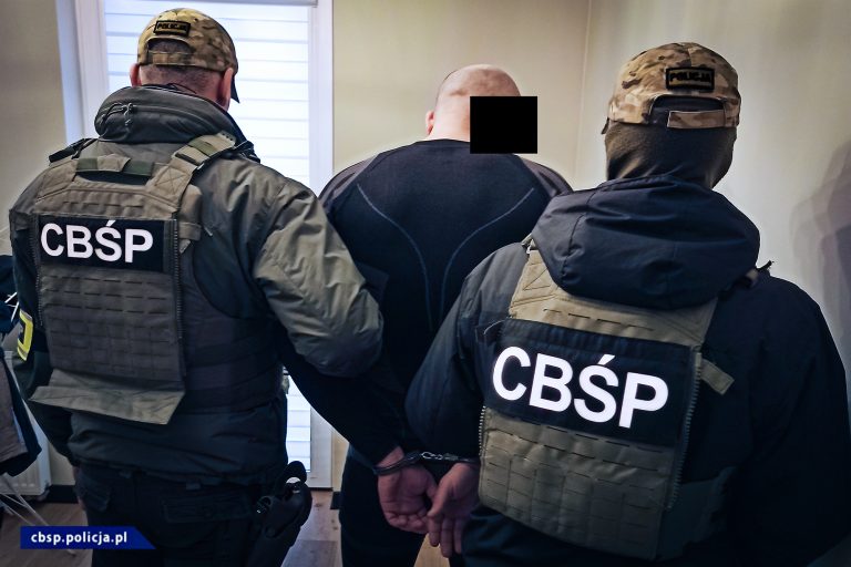 Dwaj policjanci CBŚ trzymają skutego kajdankami mężczyznę