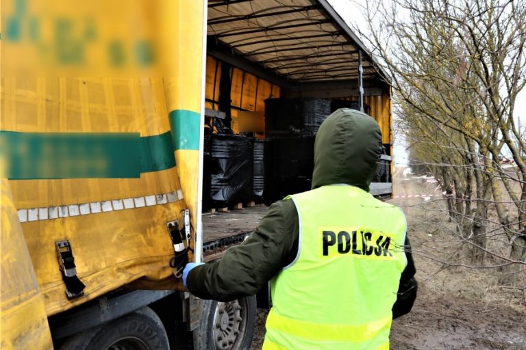 Funkcjonariusz policji stoi przy ciężarówce wypełnionej beczkami z płynem niewiadomego pochodzenia