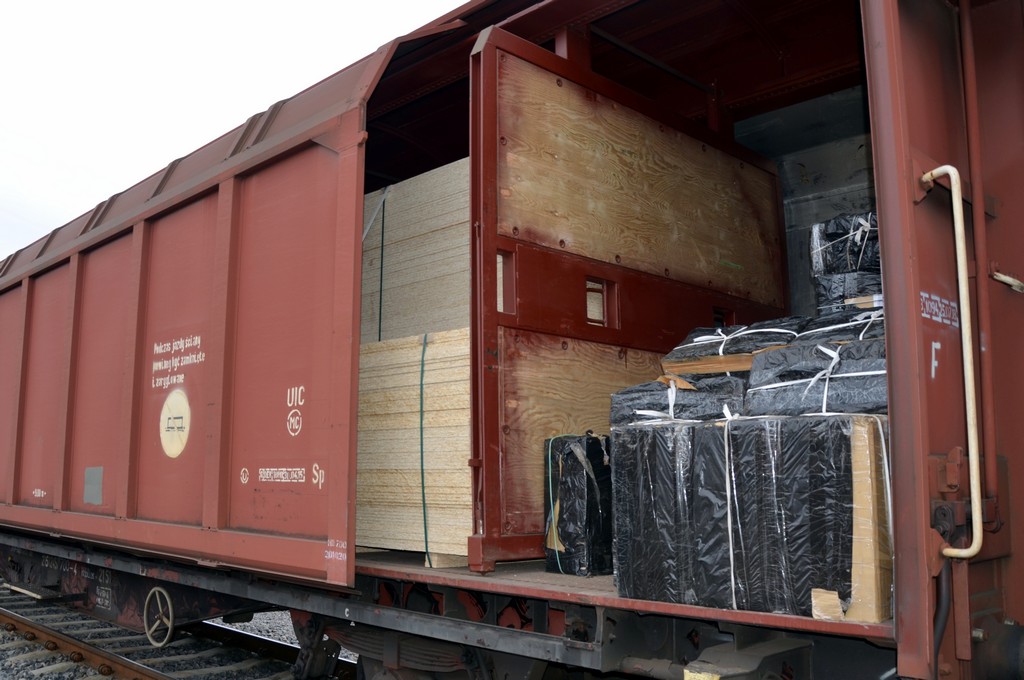 Wagon kolejowy. Wewnątrz płyta wiórowa i kartony zawinięte w czarną folię