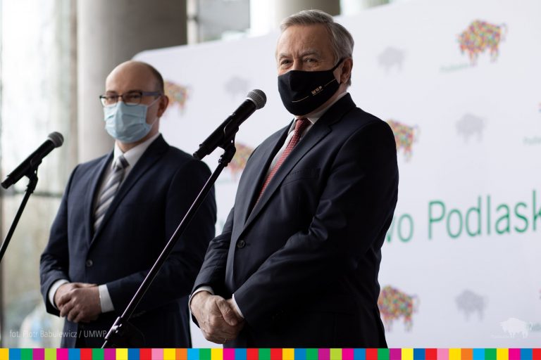 Na pierwszym planie stoi minister kultury prof. Piotr Gliński, obok niego marszałek Artur Kosicki. Mężczyźni stoją przy mikrofonach. Za nimi widoczna jest ścianka w logo województwa podlaskiego - żubra