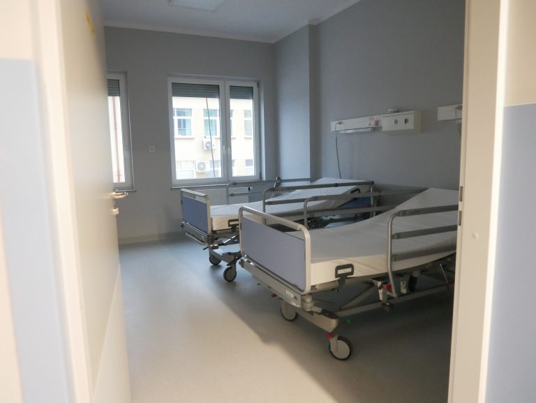 Sala szpitalna, w której stoją dwa łóżka. Na końcu sali jest okno