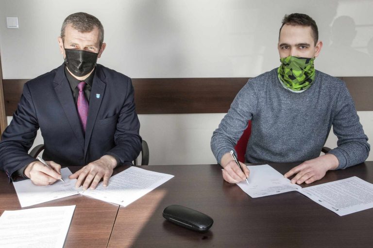 Przy stole siedzą dwaj mężczyźni podpisujący umowę o współpracy