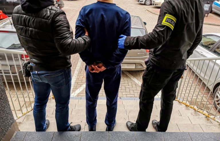 Dwaj policjanci trzymają skutego kajdankami mężczyznę.