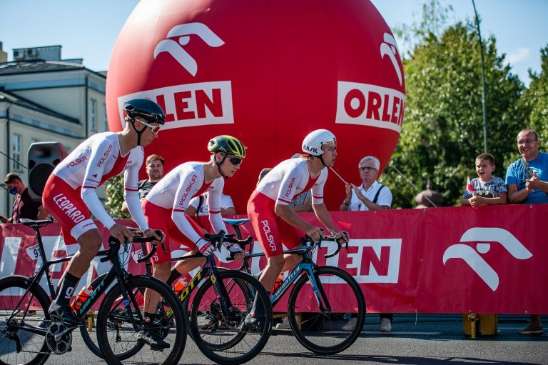 Trzej kolarze reprezentacji narodowej Polski przejeżdżają na rowerach koło kibiców