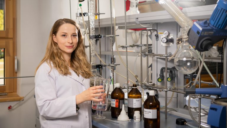 Młoda badaczka chemii stoi w białym fartuchu w pracowni