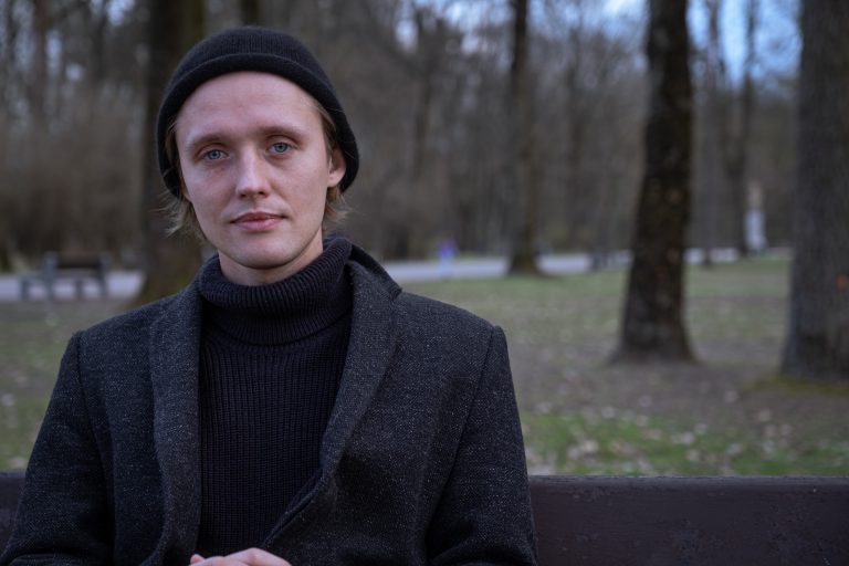 Aktor Bartosz Bielenia siedzi na ławce w parku
