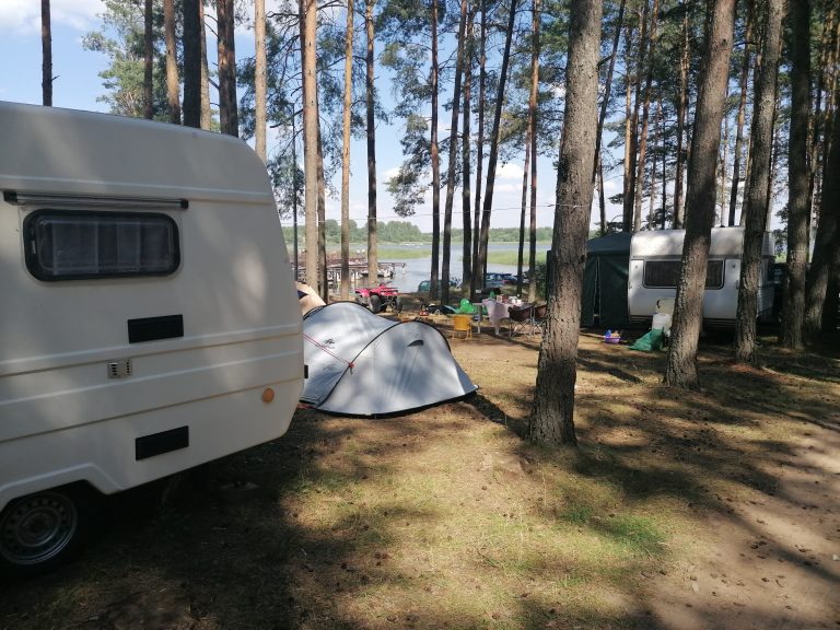 Skraj lasu, na polanie rozbity namiot i przyczepa kempingowa