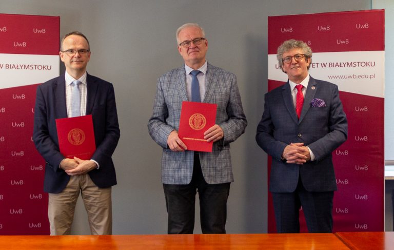 Trzej mężczyźni stoją z teczkami, w tle widać banery promujące białostocką uczelnię