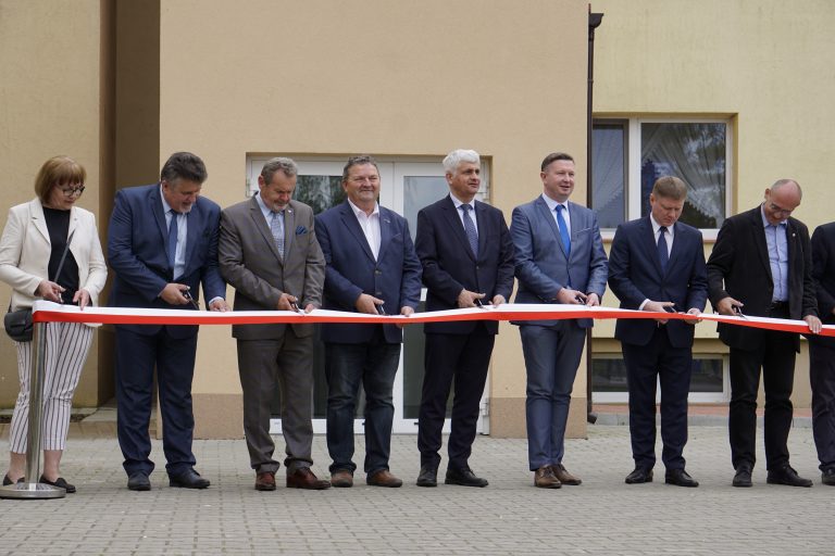 Mężczyźni stojący w rzędzie przecinają biało - czerwoną wstęgę