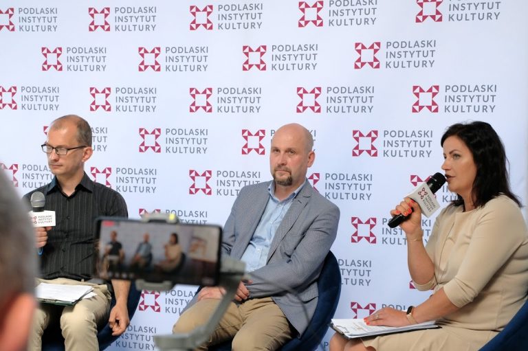 Trzy osoby siedzą na tle ścianki Podlaskiego Instytutu Kultury