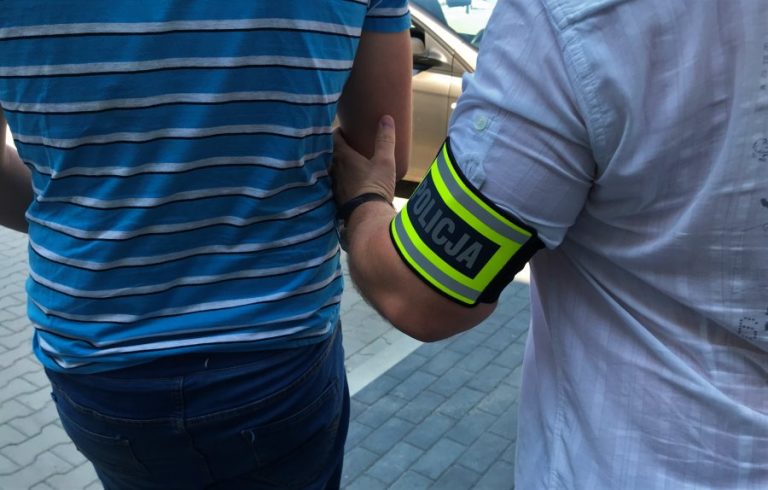 Policjant trzyma pod rękę aresztowanego mężczyznę