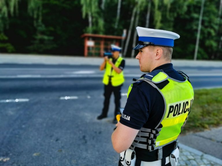 Dwaj policjanci przy drodze, jeden z nich trzyma w ręce miernik prędkości