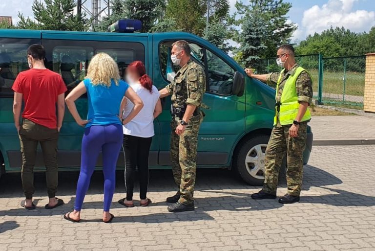 Cudzoziemcy stoją przy pojeździe służbowym POSG