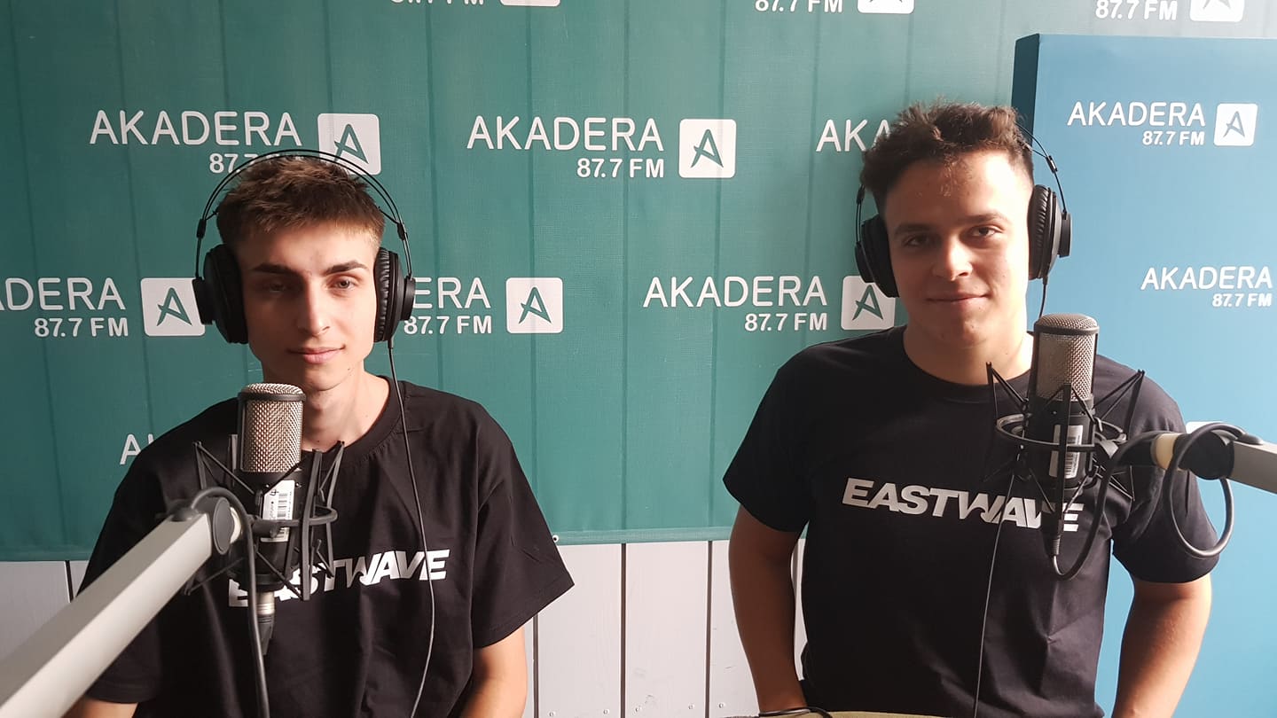 Na tle zielonej ściany w napisy Akadera, przy mikrofonach siedzi dwóch chłopaków w czarnych koszulkach z napisem: East Wave
