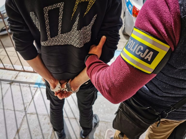 Policjant trzyma za rękę skutego kajdankami mężczyznę