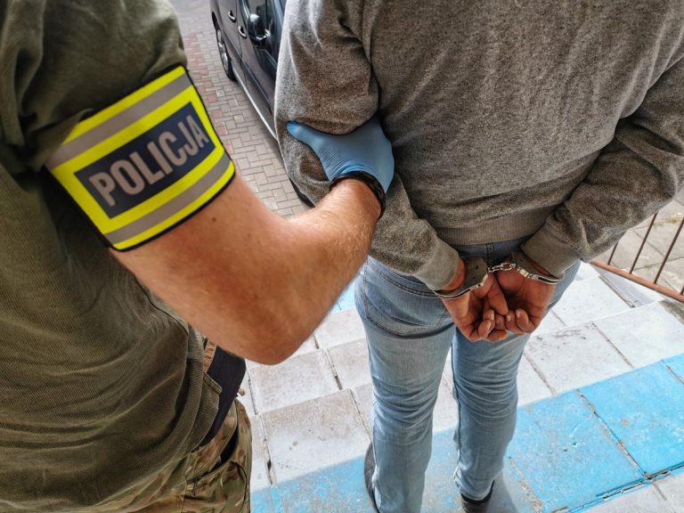 Policjant trzyma skutego kajdankami mężczyznę