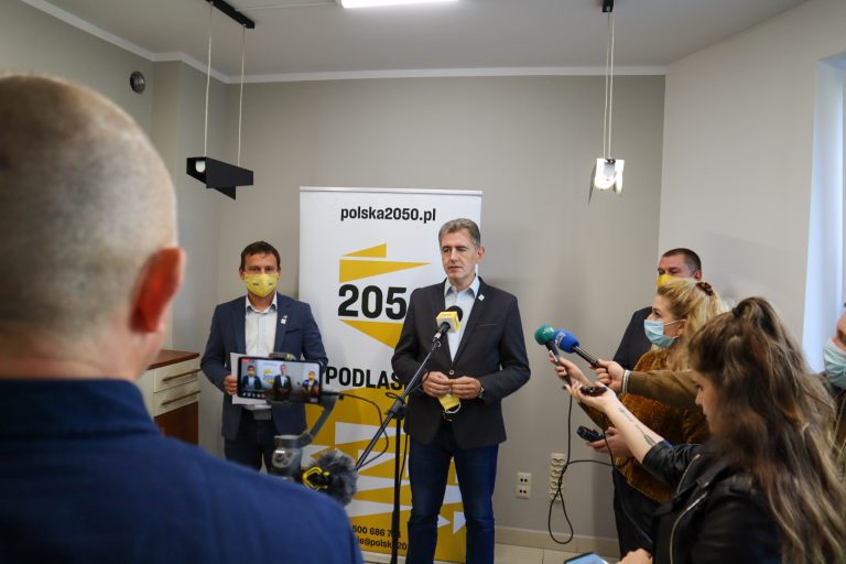Na standzie Polska 2050 stoi dwóch mężczyzn, wokół nich są dziennikarze