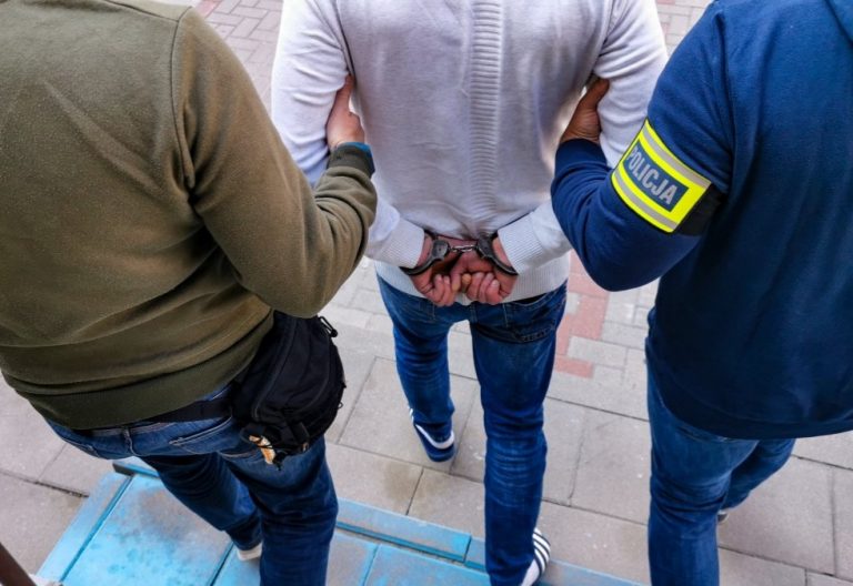 Dwaj policjanci prowadzą skutego kajdankami mężczyznę