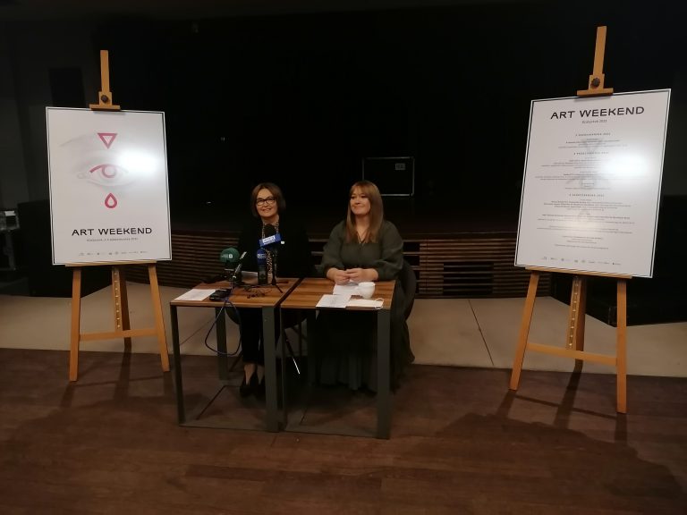 Konferencja prasowa. Przy stole zastawionym mikrofonami siedzą dwie kobiety. Obok na sztalugach wiszą plakaty promujące wydarzenie kulturalne