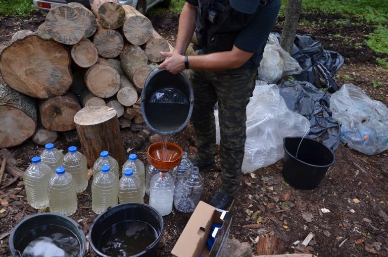 Funkcjonariusz KAS przelewa alkohol z wiadra do butelki