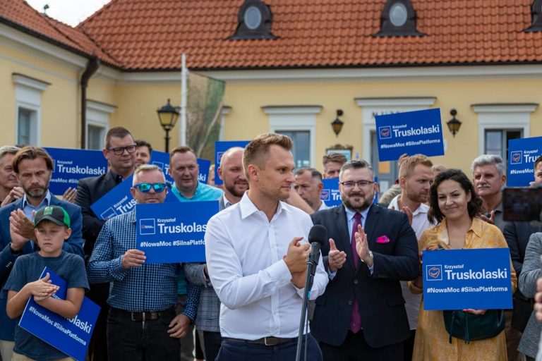 Na tle białostockiego Ratusza stoi grupa ludzi. Osoby te trzymają niebieski tabliczki z napisem: Krzysztof Truskolaski. Na przedzie, przed tymi ludźmi stoi poseł Koalicji Obywatelskiej Krzysztof Truskolaski